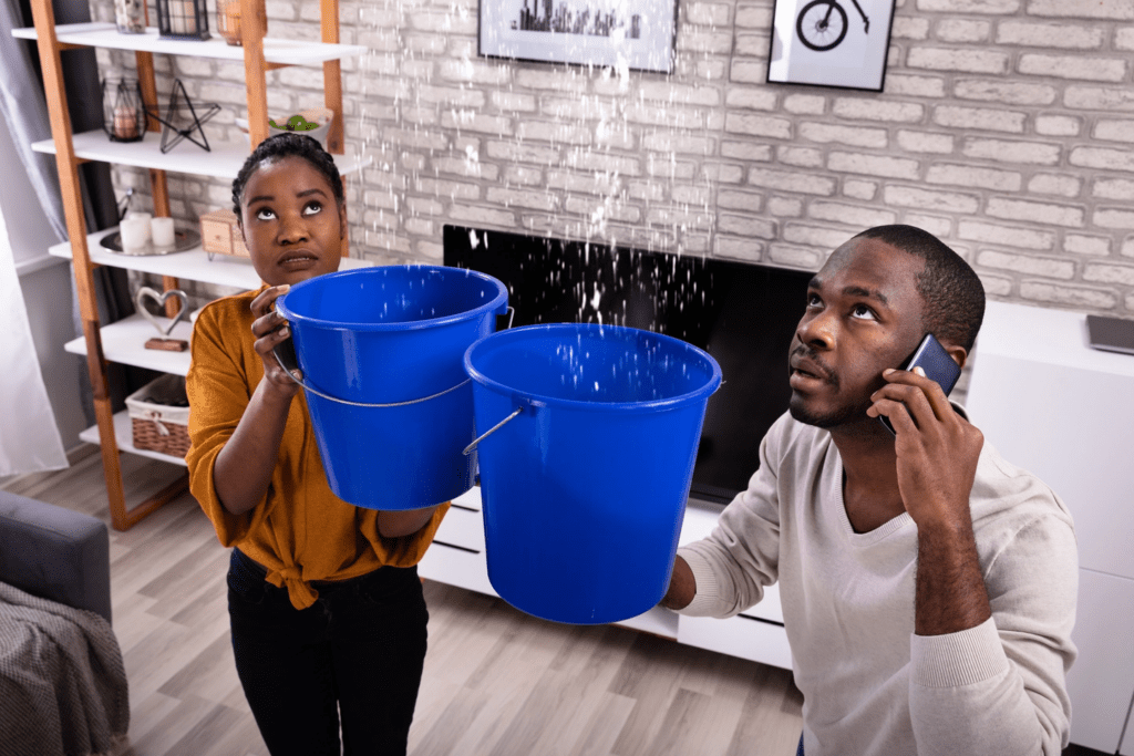 A young couple holding water buckets inside their living room capturing water from the cieling